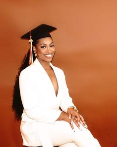 a woman in a graduation cap and gown sitting on a stool with her legs crossed