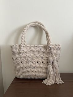 a white woven bag sitting on top of a wooden table next to a planter