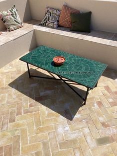 a green table sitting on top of a tiled floor next to a bench with pillows