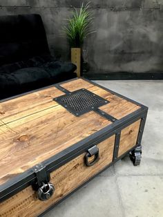 a large wooden trunk sitting on top of a floor next to a black couch and potted plant