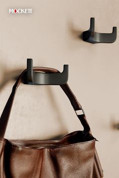 a brown purse hanging on the wall with two hooks attached to it's sides