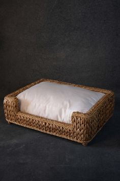 a dog bed made out of wicker with white pillows on the bottom and sides