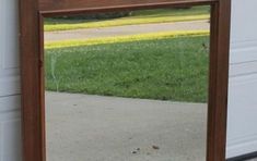 a mirror sitting on the side of a building next to a grass covered yard and sidewalk