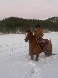 a woman riding on the back of a brown horse in snow next to a fence