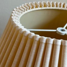 a close up of a lamp shade with a white button on the bottom and light brown pleated lampshade