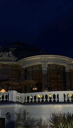 a clock tower is lit up in front of a large building with many windows and balconies