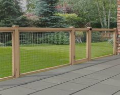 a wooden fence with wire around it on the side of a brick wall in front of a green yard