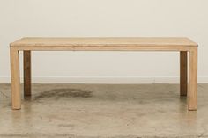 a wooden table sitting on top of a cement floor next to a white painted wall