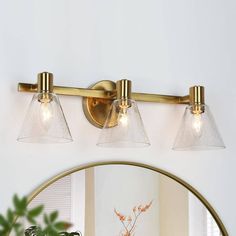 three light bathroom fixture with clear glass shades on the wall and gold trimmings