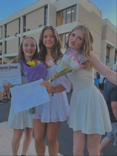 three girls are holding flowers and posing for the camera