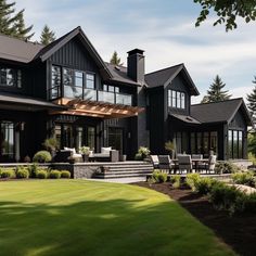 a large black house with lots of windows on the front and side of it, surrounded by lush green grass