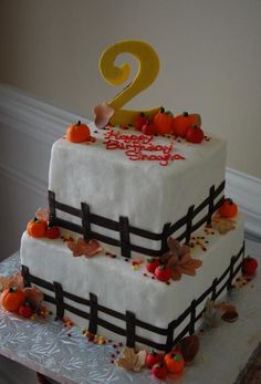 a two tiered birthday cake with pumpkins and leaves on the top, sitting on a table