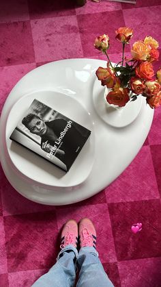 a person's feet on a table with a magazine and flowers in a vase