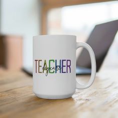 a white coffee mug sitting on top of a wooden table next to a laptop computer