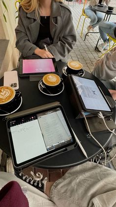 a woman sitting at a table with two ipads on it and coffee cups in front of her