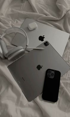 an apple phone, headphones and laptop on a bed with white sheets in the background