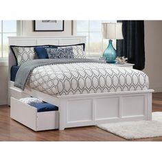 a white bed with drawers underneath it and a blue vase on the nightstand next to it