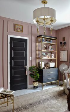 a living room with pink walls and gold trim on the doors, shelving unit