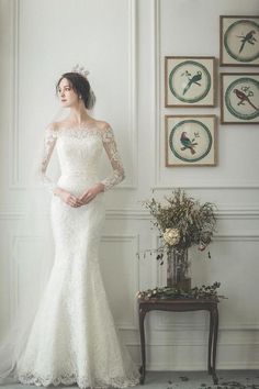 a woman in a white wedding dress standing next to a wall with pictures on it