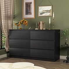 a black dresser sitting in a living room next to a window with sunflowers on it