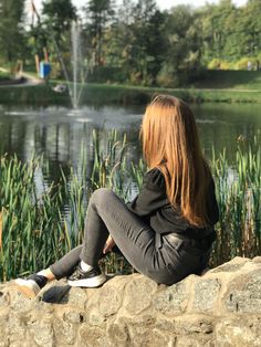 a woman sitting on the edge of a stone wall next to a pond