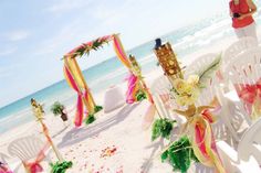 an outdoor wedding setup on the beach with white chairs and pink sashes draped over them