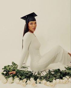 a woman wearing a graduation cap sitting on the ground with flowers in front of her