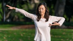 a woman standing in the grass holding her arms out with both hands and looking at something