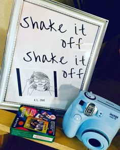 a blue camera sitting on top of a wooden table next to a sign that says shake it off snake it off