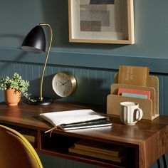 a wooden desk topped with a laptop computer next to a lamp and books on top of it