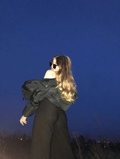 a woman in black dress and sunglasses looking up at the sky