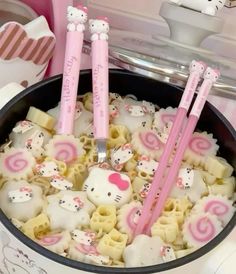 three hello kitty utensils sitting in a pot filled with noodles and other food