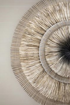 a circular sculpture made out of metal rods and wood sticks on a wall in front of a white background