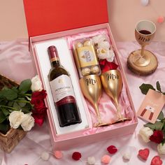 two wine glasses and a bottle in a pink gift box with rose petals on the table