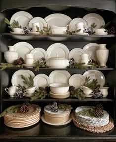 a black china cabinet filled with dishes and pine cones