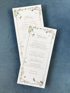 two wedding programs with flowers and gold trim on blue velvete paper, one is folded in