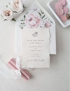 a wedding save the date card with pink flowers on it next to some cookies and marshmallows