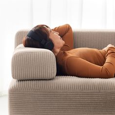 a woman laying on top of a green couch with headphones in her ears and eyes closed