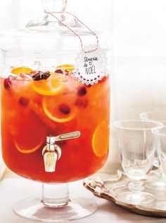 a glass jar filled with liquid and orange slices on top of a table next to glasses