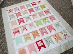 a quilt is laying on the floor in front of a wall hanging with bunting