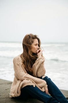 a woman is sitting on the beach talking on her cell phone and looking off into the distance