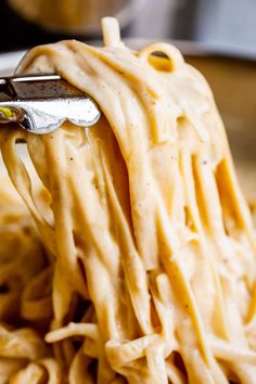 a fork full of pasta being held up by someone's hand in a bowl