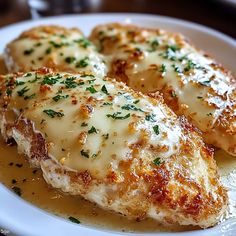 two pieces of chicken covered in gravy on a white plate with parmesan cheese