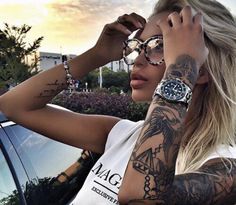 a woman with tattoos on her arms and arm is leaning against a car window while wearing glasses