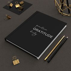 a black book with gold lettering on it next to two golden objects and a pen