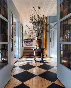 a large vase with some flowers in it on a checkered wooden floor next to windows