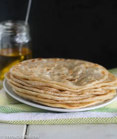 a stack of flatbreads on a plate next to a jar of oil and a spoon