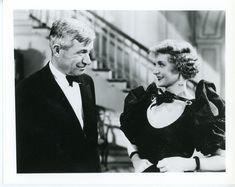 an old black and white photo of two people in formal wear talking to each other