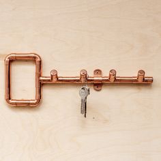 a metal key is attached to a wooden wall with copper pipe fittings on it