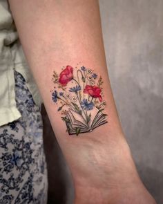 a woman's arm with a book and flowers tattoo on the left side of her wrist